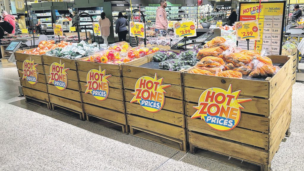 Displays marked with “Hot Zone Prices” signage feature easy-to-grab bagged items, including yellow onions, Haas avocados, red and yellow peppers, mini cucumbers and russet potatoes.
