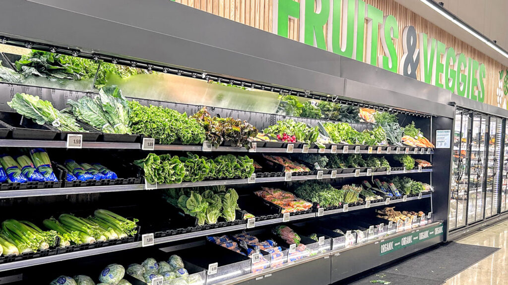 At the produce department’s front open section, displays highlight head lettuce, loose greens, radishes and bagged celery.