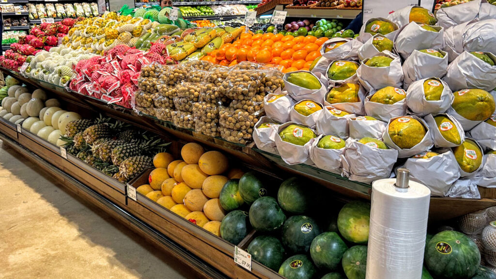 Behind a papaya display, there are mixed Asian and tropical fruits, ranging from mangos to dragon fruit, with melons and pineapples mixed into the bottom of the display.